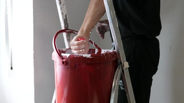 Painter Carrying Red Paint Bucket on Ladder Preparing Interior Wall Renovation Project Home Improvement Close Up Handwork Concept Real Estate