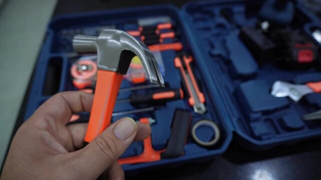Hand technician in work holding an hammer. Video. Macro close-up hand man holds an hammer and, with a tool case in the background. Young man with hammer. Shot of tools, anvil, Small hammer, pliers.