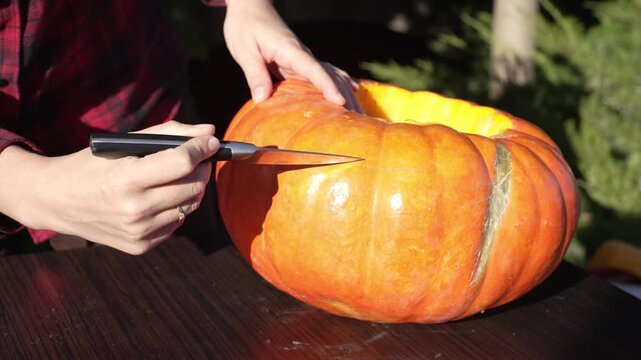 Woman marking and scoring outline of spooky eyes on orange pumpkin with knife at sunset, static 4k 60fps slow motion footage