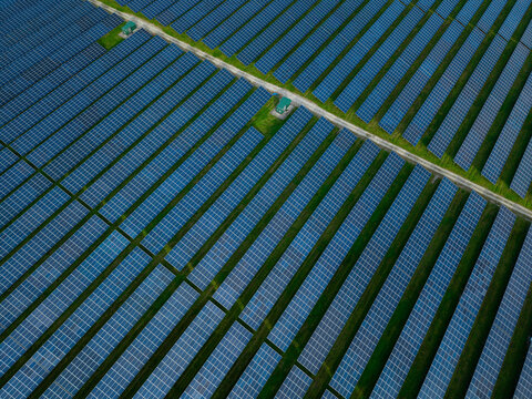 Aerial view of a large solar farm with rows of photovoltaic panels and green grass strips in Deeside, Wales, United Kingdom.
