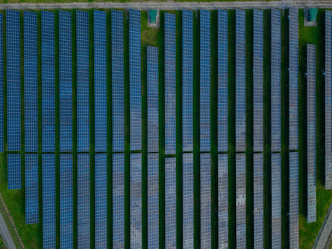 Aerial view of rows of solar panels arranged in a solar farm with green grass strips in Deeside, Wales, United Kingdom.