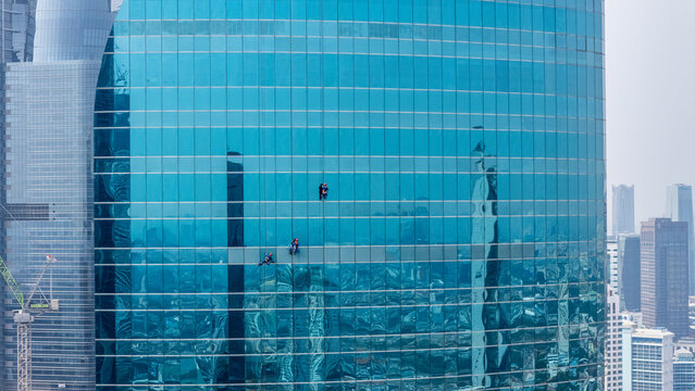 Aerial view of window cleaners suspended on ropes cleaning the glass facade of a modern skyscraper in Jakarta, Indonesia.