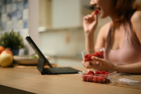 Cropped of Woman Eating Fresh Raspberries with Antioxidant Benefits While Using Tablet in Kitchen, Healthy Snack Lifestyle