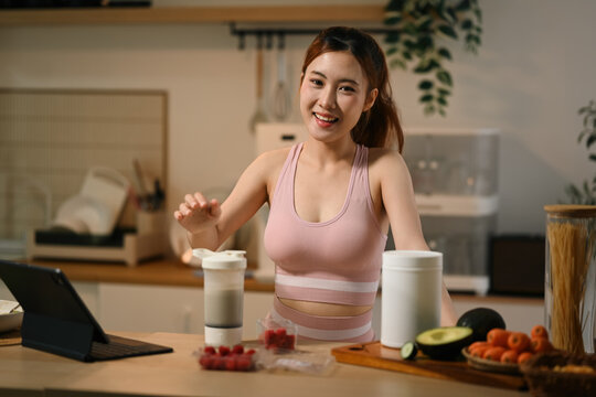 Young Asian Woman Preparing Raspberry Protein Shake with Antioxidant Supplements in Kitchen for Skin Nourishment and Anti Aging