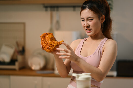 Young Asian Woman in Sportswear Refusing Fried Chicken While on Diet in Kitchen