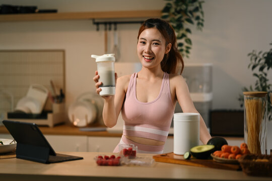 Asian Woman in Sportswear Holding Protein Shaker with Raspberries and Supplements in Kitchen