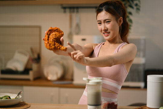 Young Asian Woman in Sportswear Refusing Fried Chicken While on Diet in Kitchen
