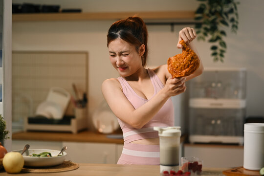 Asian Woman in Sportswear Refusing Fried Chicken While on Diet in Modern Kitchen