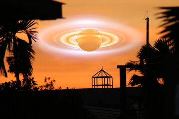 Saturn shadow near earth on the gray sky and silhouette architecture on the sunset orange cloud © darkfoxelixir