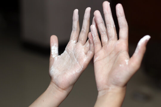 Both palms of a person raised up, covered in fine white powder or flour against a dark background