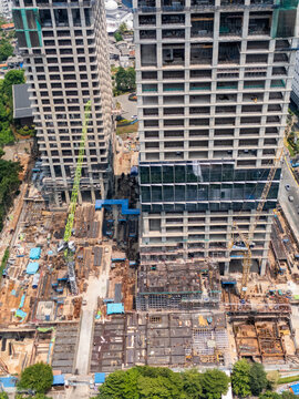 Aerial view of a large construction site featuring two towering skyscrapers under development with multiple cranes, exposed steel reinforcement, and concrete foundations in Jakarta, Indonesia.