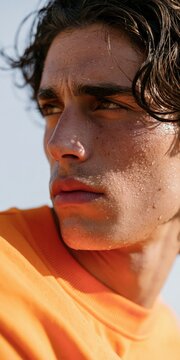 Close up profile portrait of young man with water droplets and sandy skin in orange sweater during golden hour for banner background and fashion layout