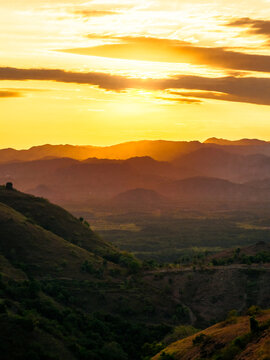 Aerial view of rolling hills and mountainous landscape at sunset with golden light illuminating the horizon, Flores, East Nusa Tenggara, Indonesia.
