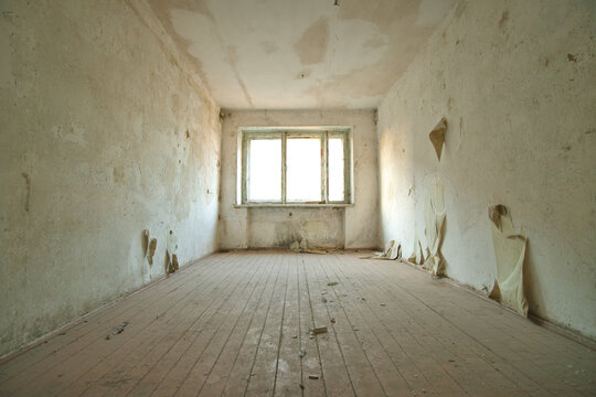 Empty abandoned room interior with old wooden plank floor and peeling wallpaper on dirty walls. Damaged neglected house apartment