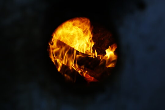 Bright golden flames blaze through a round furnace peephole.
