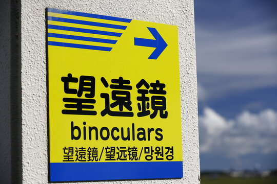 A bright yellow directional signboard guides visitors toward viewing binoculars.