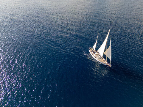 Aerial view of a white sailboat with sails unfurled sailing on the deep blue Mediterranean Sea in Moraira, Valencian Community, Spain.