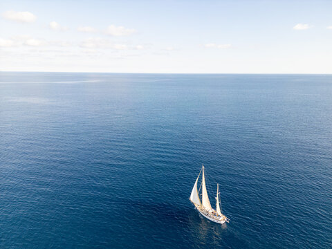 Aerial view of a white sailboat sailing on the deep blue Mediterranean Sea near the coast of Moraira, Valencian Community, Spain.
