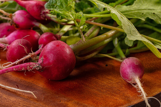 Fresh vegetable harvest featuring red radish roots and green leafy stems on wooden surface
