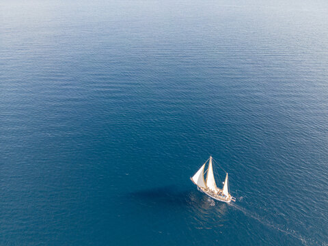Aerial view of a white sailboat sailing on the deep blue Mediterranean Sea off the coast of Moraira, Valencian Community, Spain.