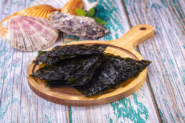 Crispy dark green nori seaweed chips on round wooden board with seashells and oyster, dried algae snack © Andrei Starostin