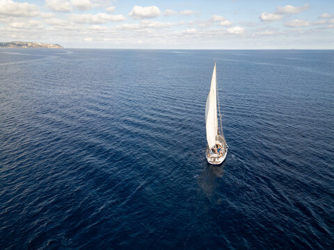 Aerial view of a sailboat sailing on the deep blue Mediterranean Sea near the coast of Moraira, Valencian Community, Spain.