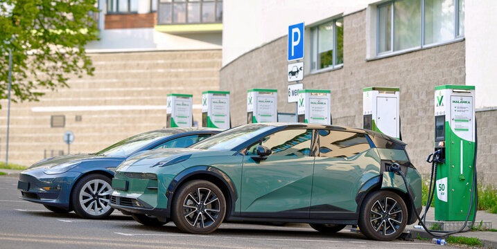 Minsk, Belarus. May 15, 2024. Electric cars, Tesla and green Zeekr, parked side by side at row of charging stations Malanka in an urban parking lot, electric vehicles plugged into charging stations