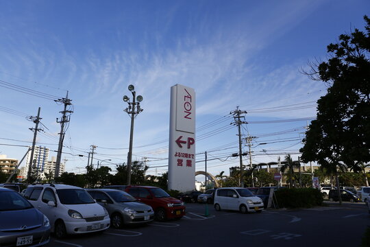 An AEON shopping mall parking lot sign stands tall under a clear blue sky.