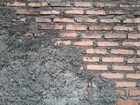 Unfinished red brick wall partially covered with rough gray cement plaster, uneven textured surface under construction, full frame grunge background
