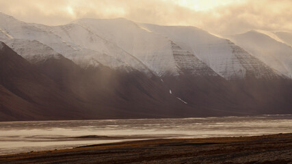 Snow-dusted layered mountains in soft hazy golden light, Svalbard, Norway © Arnaud