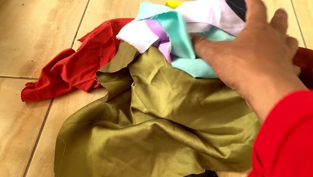 Hand rummaging through a pile of colorful fabric scraps and textile remnants.