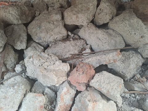 Close-up of broken gray porous concrete chunks with a single red brick fragment and thin rebar, demolition rubble texture background, full frame