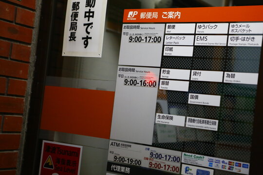 Service hours information board and tsunami advisory sign posted on the entrance of a Japan Post office.