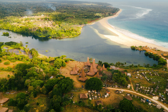 Aerial view of Pantai Ratenggaro featuring traditional Sumba houses with high thatched roofs, a river estuary, and white sand beach in Kodi Bangedo, East Nusa Tenggara, Indonesia.