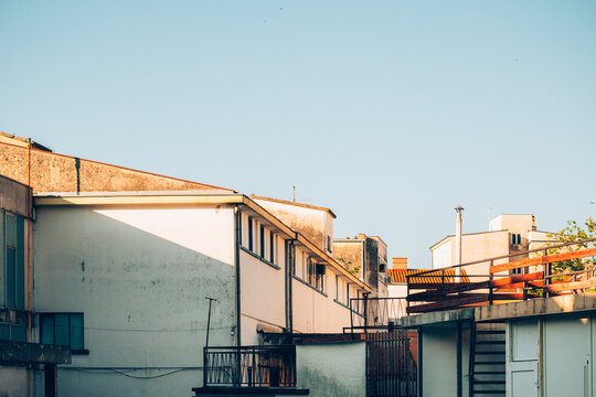 Weathered urban building facades and rooftops illuminated by warm late afternoon sunlight with harsh geometric shadows.
