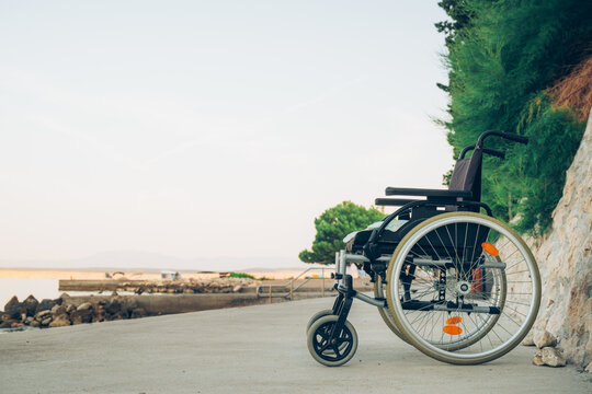 Empty wheelchair parked beside quiet seaside promenade overlooking calm Adriatic coast at sunset. Accessibility, disability inclusion, mobility and peaceful coastal travel concept.