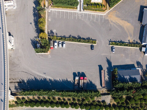 Aerial view of a paved parking lot with several parked cars and trucks, bordered by rows of trees and a bridge structure in Istanbul, Istanbul, Turkiye.