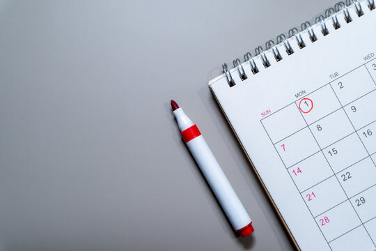Spiral desk calendar with Monday the first circled in red beside a matching marker with copy space. Planning, scheduling, deadlines, appointments, and new beginnings concept.