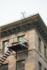 Metal fire escape and ladder on the corner of an old stone building with ornate cornice © Valeriia