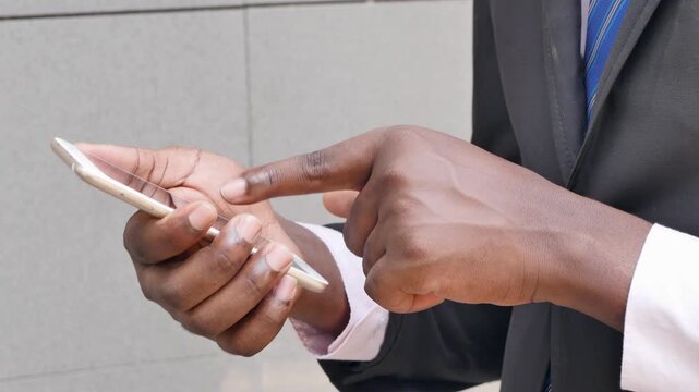 Closeup of a 20s young adult black African businessman's hand using a smartphone outdoors in an urban office setting, real human hand movement, side view
