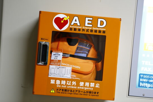 An orange wall-mounted AED emergency cabinet housing a portable defibrillator unit inside a transit station.