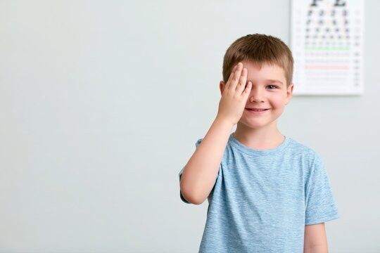 Smiling boy covering one eye during a vision test, cheerful child patient beside an eye chart with copy space