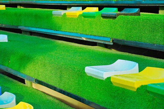 Colorful seating area with green artificial grass and bright plastic seats in various colors. Ideal for outdoor events or sports venues.