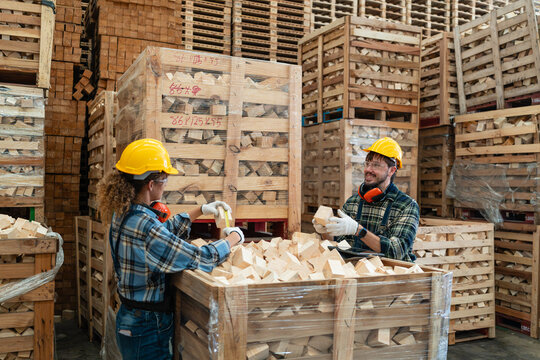 During wood offcut checks beside a crate, two colleagues take measurements with a tape measure and consult a tablet.