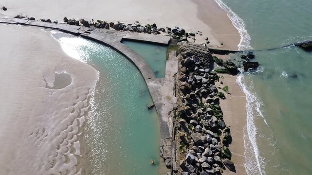 Static aerial view of tidal pool and seawall facing Soulac
