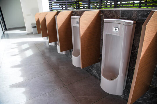 Row of modern white ceramic urinals with automatic sensors on dark marble wall in public restroom