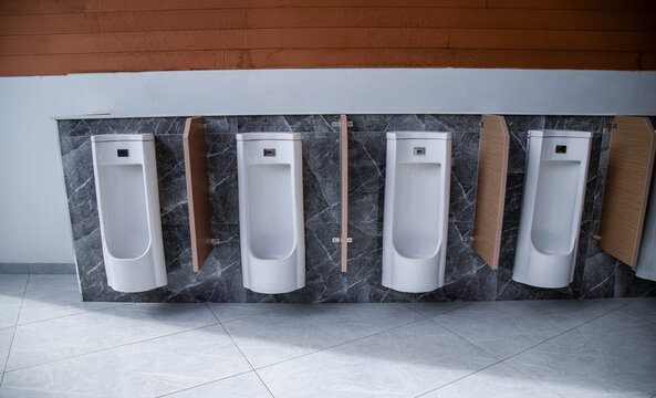 Row of modern white ceramic urinals with automatic sensors on dark marble wall in public restroom