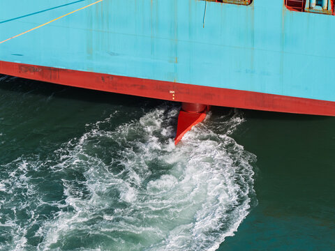Aerial view of a red ship rudder creating a white wake in the sea alongside a blue hull in the United Kingdom.