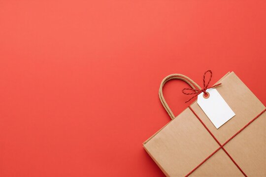 Kraft paper shopping bag with blank white tag and red string on red background, shopping concept with large copy space