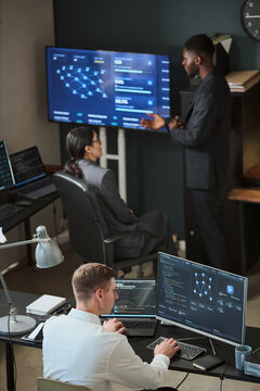 Vertical shot of diverse colleagues analyzing network security data on screens in cybersecurity office. Image suitable for enterprise data protection campaigns